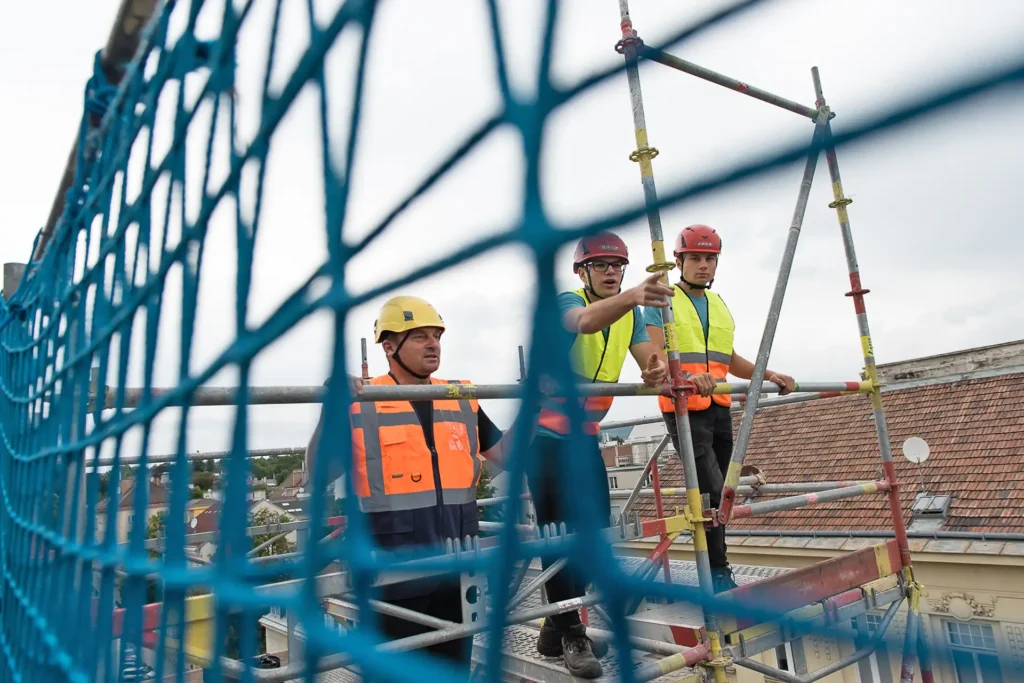 Drei Männer in Sicherheitswesten stehen auf einem Gerüst