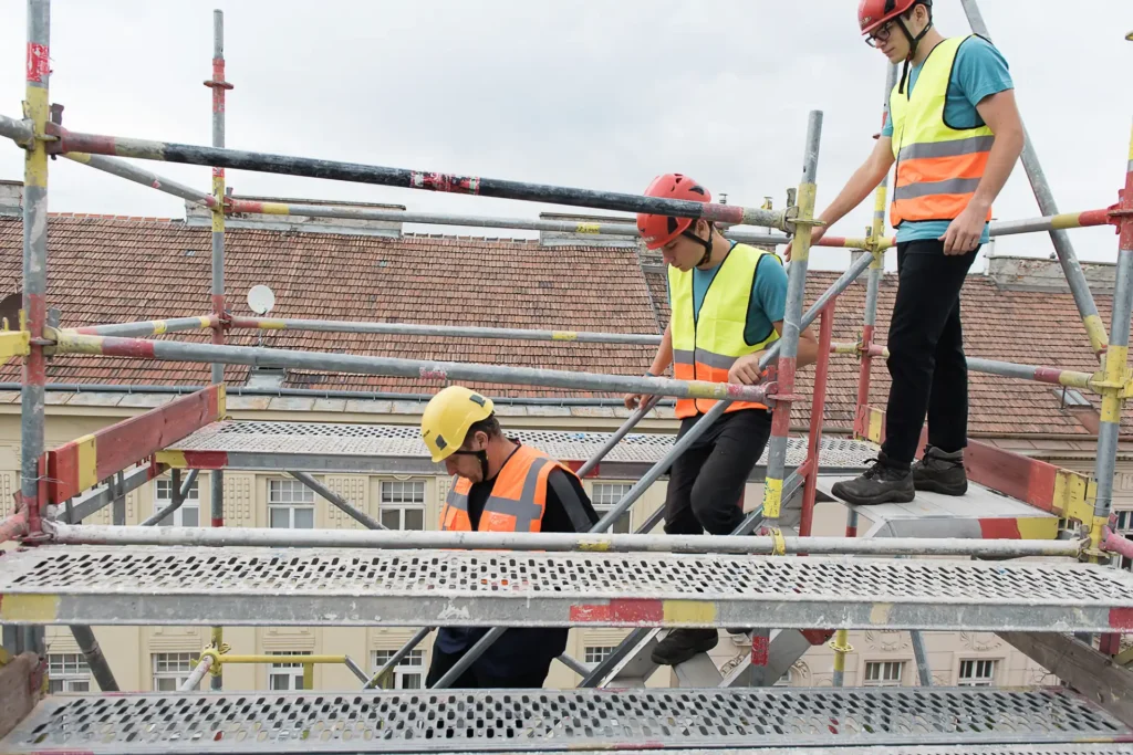 Drei Männer mit Sicherheitswesten stehen auf einem Gerüst